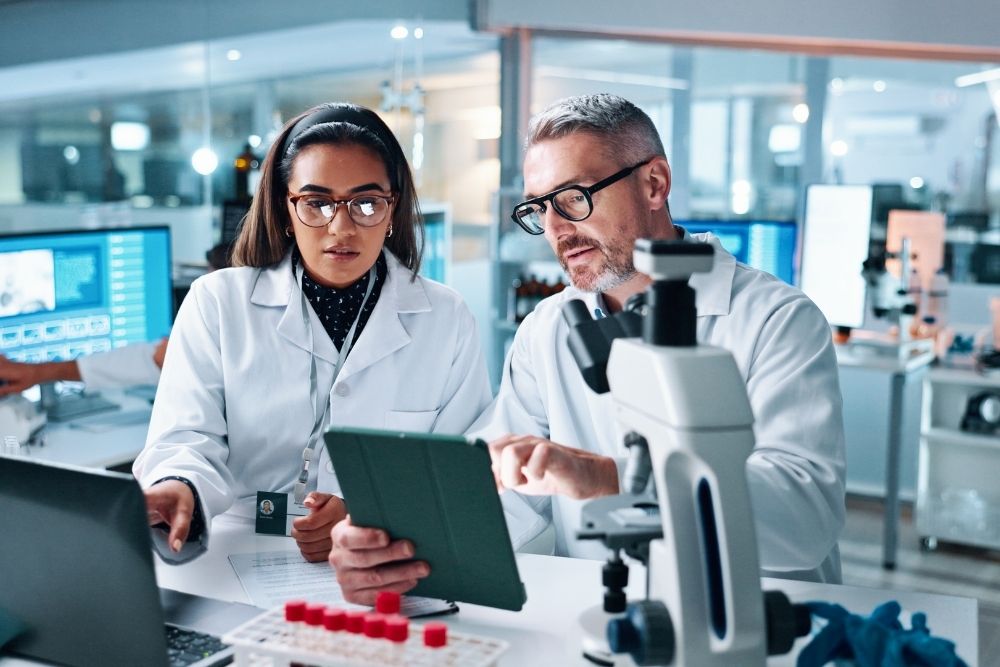 Two scientists in lab coats collaborating in a laboratory, looking at a tablet computer.